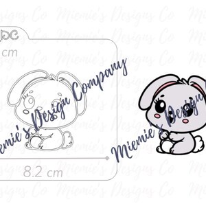 May include: A black and white line art illustration of a cute bunny rabbit sitting with its paws crossed. The bunny has large eyes and a pink nose. The image is 8.3 cm by 8.2 cm.