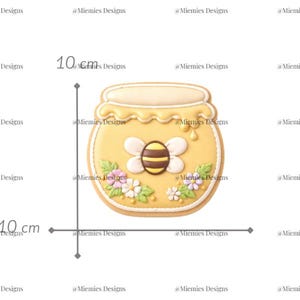 May include: A honey pot-shaped biscuit, approximately 10 cm tall and wide, decorated with yellow icing and a bee. The biscuit is adorned with white and pink flowers and the text "MDC 151".