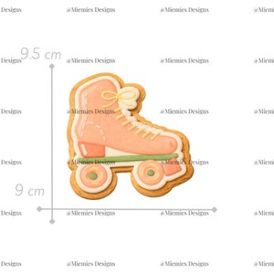 Puede incluir: Un cortador de galletas con forma de patín, de aproximadamente 9,5 cm de alto y 9 cm de ancho, con un glaseado naranja claro y detalles decorativos. El cortador tiene un contorno marrón claro y detalles verdes. El texto "MDC 013" es visible.