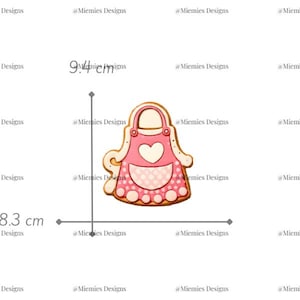 Puede incluir: Un cortador de galletas en forma de delantal rosa con diseño de corazón, de 8,3 cm de ancho y 9,4 cm de alto. El cortador tiene un delantal rosa claro con un corazón blanco y un estampado de lunares. El texto "MDC 198" es visible.