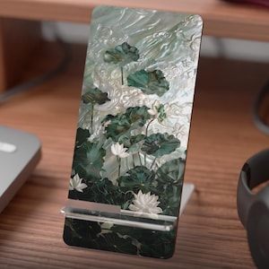 May include: A white phone stand with a green and white floral design. The stand is made of a flat, printed material and has a small kickstand.