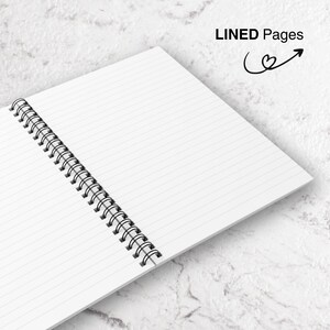 May include: Open spiral notebook with lined pages. The notebook is open to reveal the white pages with horizontal lines. The binding is a black metal spiral. The words "LINED Pages" are printed in black, with a heart and arrow graphic.