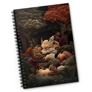 May include: A spiral-bound notebook featuring a textured illustration of a fox curled up in a forest setting. The scene includes deep orange, brown, and muted green foliage, along with two pumpkins nestled among the leaves against a dark background.