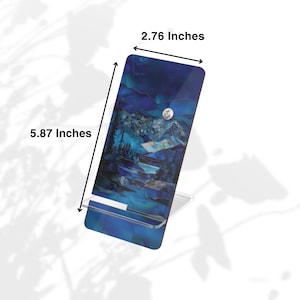 May include: A rectangular phone stand with a blue and white mountain landscape design. The stand is 5.87 inches tall and 2.76 inches wide. The stand is made of a clear material and is designed to hold a phone or tablet.