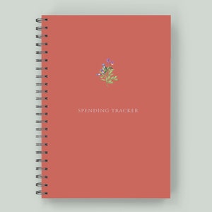 May include: A coral-colored spiral bound notebook with the text "SPENDING TRACKER" and a small floral illustration.