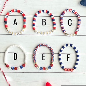 K&ouml;nnte beinhalten: Sechs Armb&auml;nder mit roten, wei&szlig;en und blauen Perlen. Die Armb&auml;nder buchstabieren "America", "Freedom", "USA", "America", "Freedom" und "USA".