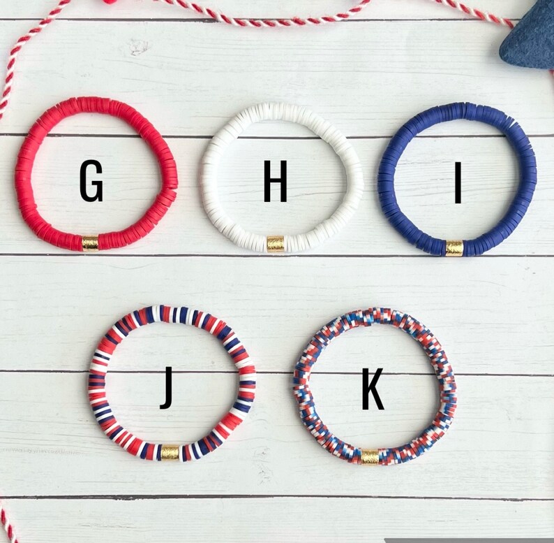 K&ouml;nnte beinhalten: F&uuml;nf bunte Armb&auml;nder mit goldenen Akzenten. Die Armb&auml;nder sind rot, wei&szlig;, blau und eine Kombination aus rot, wei&szlig; und blau. Die Armb&auml;nder sind mit G, H, I, J und K beschriftet.