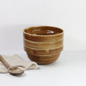 May include: A stack of four brown ceramic mixing bowls with a striped pattern. The bowls are stacked on a white surface.