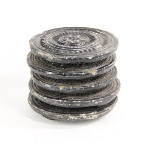 May include: A stack of six black round coasters with intricate carved designs. The coasters are made of a dark wood or stone material.