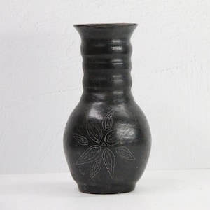 May include: A black ceramic vase with a carved flower design. The vase has a narrow neck and a wide, rounded base.
