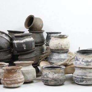 May include: A collection of various sized, round, ceramic pots in shades of brown, black, and white. Some pots have a distressed, aged look.
