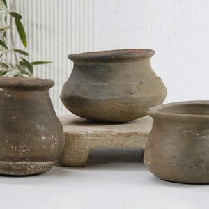 May include: Three brown clay pots of varying sizes and shapes. The pots are unglazed and have a rustic, earthy appearance.