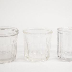 May include: Three clear glass jars with a ribbed design. The jars are empty and have a round shape.