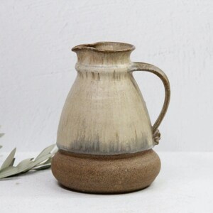 May include: A ceramic pitcher with a light brown glaze and a brown base. The pitcher has a wide mouth and a handle.