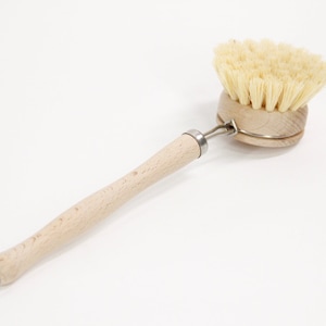 May include: A wooden-handled dish brush with natural bristles. The brush has a metal ring connecting the handle to the brush head.