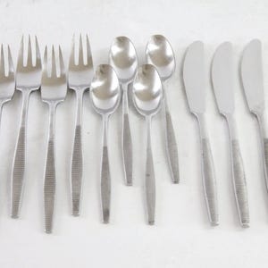May include: A collection of stainless steel flatware, including forks, spoons, and knives. The utensils have a simple, modern design with textured handles. The arrangement suggests a formal dining setting, perfect for a dinner party or special occasion.