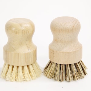 May include: Two wooden handled scrub brushes with natural bristles. The brush on the left has light colored bristles and the brush on the right has darker bristles.
