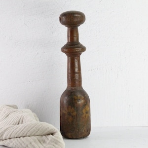 May include: A vintage wooden potato masher with a rounded top and a long, slender handle. The masher has a dark brown color and shows signs of wear and age.