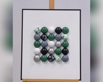 May include: A white canvas with a grid of 25 round, colorful ornaments. The ornaments are in shades of green, gray, white, and black. Some of the ornaments have a marbled pattern.