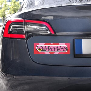 May include: A rectangular bumper sticker with the text "FUCK AROUND and FIND OUT" in a stylized font. The sticker has a red background with pink hearts and stars.