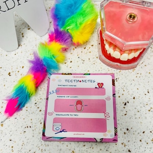 May include: A vibrant pen with a rainbow-coloured fluffy top and a pink notepad with the text "TOOTH NOTES" and areas for patient information. A dental model and a tooth-shaped cutout are also visible.