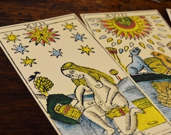 May include: Three tarot cards, the first card shows a woman with long blonde hair, the second card shows a sun with a face, and the third card shows a creature with a long tail.
