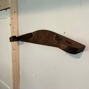 Op de afbeelding: Een donker gebeitst houten wandrek met een gebogen ontwerp. De plank heeft twee verzonken delen en is aan een witte muur bevestigd. De plank is ongeveer 76 cm lang.
