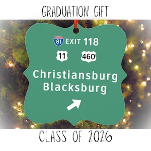 May include: A green metal ornament shaped like a road sign, with the text "GRADUATION GIFT" at the top and "CLASS OF 2026" at the bottom. The sign features highway numbers and the names Christiansburg and Blacksburg.