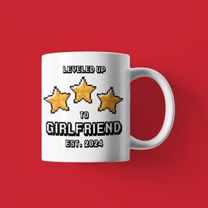 May include: White ceramic mug with a pixelated design that says "LEVELED UP TO GIRLFRIEND EST. 2024" with three gold stars.