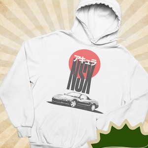 May include: White hoodie featuring a graphic of a car with the text "NSX" in a Japanese style font, set against a red circle. The hoodie has a front pocket and a hood with a drawstring.