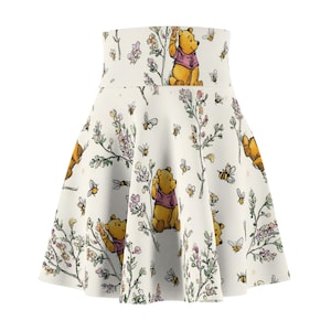 Op de afbeelding: Witte uitlopende rok met een herhalend patroon van Winnie de Poeh, bijen en bloemmotieven. De rok heeft een hoge taille en een speels ontwerp. De illustraties zijn in tinten geel, roze en groen.