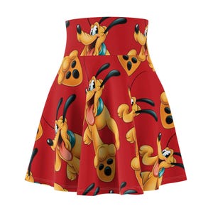 Puede incluir: Falda skater roja con un patrón repetido del personaje de dibujos animados Pluto. El diseño incluye la cara, el cuerpo y las huellas de las patas de Pluto. La falda tiene una cintura alta y una silueta acampanada.
