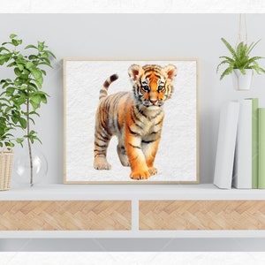 K&ouml;nnte beinhalten: Ein Aquarellbild eines niedlichen Tigerbabys mit orangefarbenen und schwarzen Streifen, das auf einem wei&szlig;en Hintergrund steht. Das Bild ist in einem hellen Holzrahmen gerahmt und auf einem wei&szlig;en Regal mit einer Holzplatte ausgestellt.