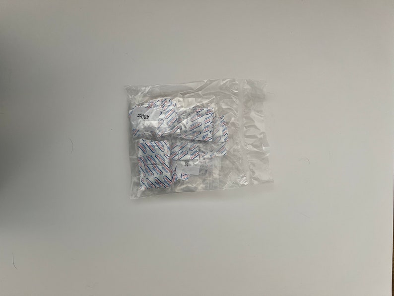May include: A clear plastic bag containing several small white packets with blue and red text. The text on the packets reads "4002C".