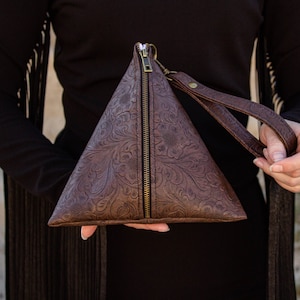 May include: A brown leather triangular clutch with a zipper closure and a floral embossed pattern. The clutch has a brown leather strap.