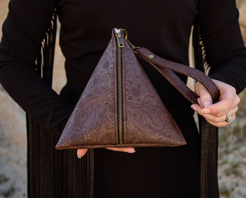 May include: A brown leather triangular clutch with a zipper closure and a floral embossed pattern. The clutch has a brown leather strap.