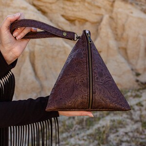 May include: A brown leather triangular purse with a zipper closure and a floral embossed design. The purse has a brown leather strap.