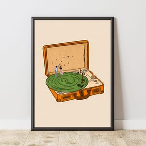 May include: An orange suitcase-shaped record player with a green record and a couple dancing on it. The artwork is framed in a black frame and set against a cream-colored background. The illustration has a whimsical, romantic theme.