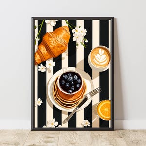 Pu&ograve; includere: Una stampa artistica incorniciata raffigurante una scena di colazione con un croissant dorato, una pila di pancake guarniti con mirtilli in una ciotolina, un latte macchiato con decorazione in schiuma e un bicchiere di succo d'arancia su sfondo a righe.