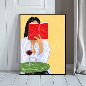 Könnte beinhalten: Ein gerahmter Kunstdruck zeigt eine Person mit dunklem Haar in einem weißen Hemd, die ein leuchtend rotes Buch vor das Gesicht hält. Ein Glas Rotwein steht auf einem runden grünen Tisch vor einem strukturierten gelben Hintergrund.