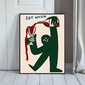 May include: A framed wall art print on a cream background featuring a dark green stylized figure pouring red wine from a bottle into a glass. The text SAY WHEN is printed in blue at the top. The illustration uses bold lines and simple shapes.