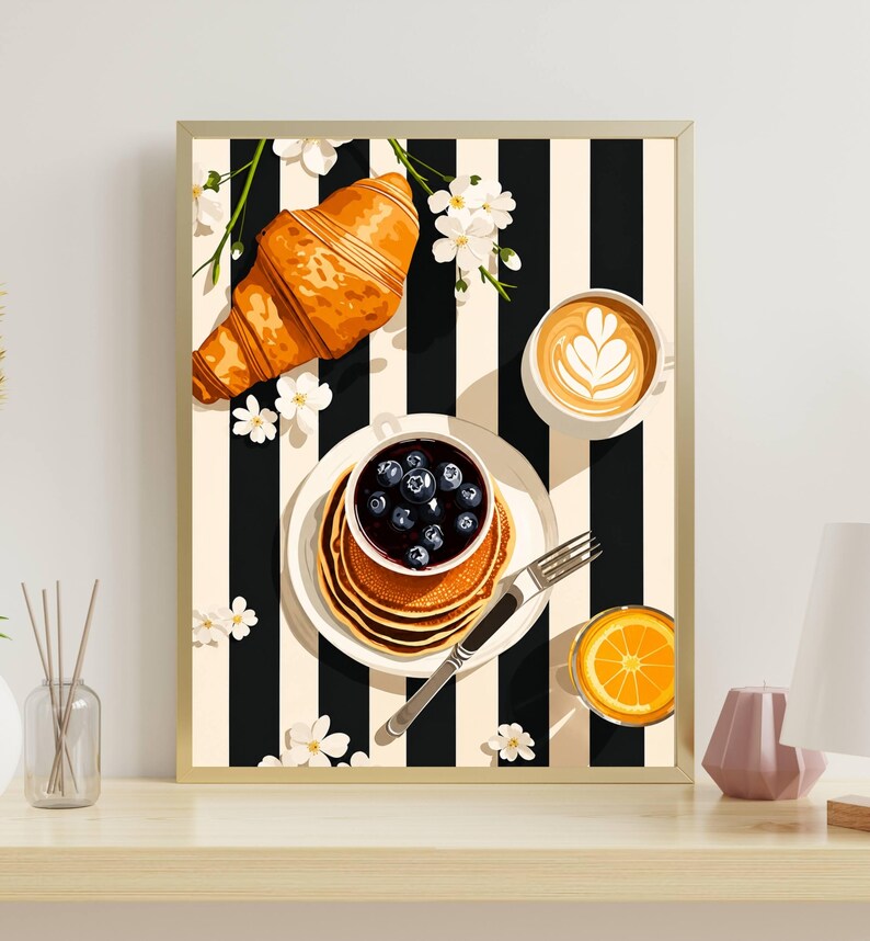 Pu&ograve; includere: Una stampa artistica incorniciata che raffigura una scena di colazione su uno sfondo a righe bianche e nere. L'immagine mostra un croissant dorato, una pila di pancake con mirtilli, una tazza di caff&egrave; con latte art e succo d'arancia.