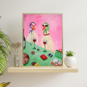 以下が含まれることがあります： サングラスとスカーフを身につけた2羽のガチョウが、テーブルでワインを楽しんでいる様子を描いた額入りの絵画。テーブルには軽食、携帯電話、そして「Sassy」と書かれた箱が置かれている。背景はピンク色。