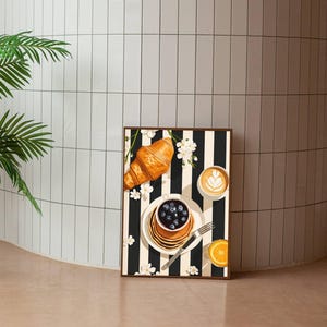 Pu&ograve; includere: Una stampa artistica rettangolare che raffigura una scena di colazione su uno sfondo a righe verticali bianche e nere. L'illustrazione include un croissant dorato, una pila di pancake con mirtilli, un latte macchiato e una fetta d'arancia.
