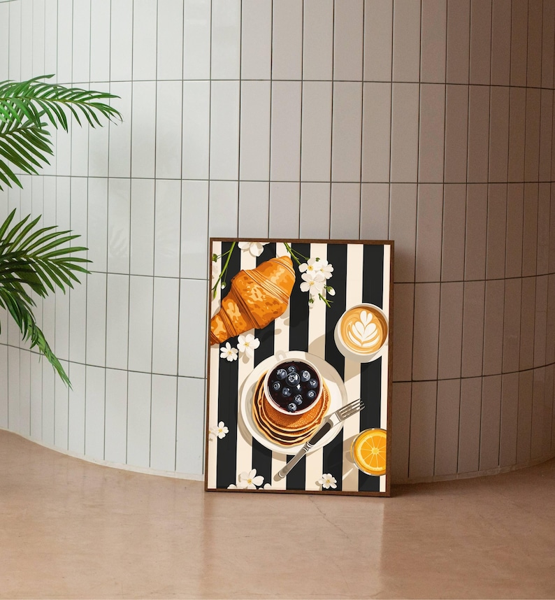 Pu&ograve; includere: Una stampa artistica rettangolare che raffigura una scena di colazione su uno sfondo a righe verticali bianche e nere. L'illustrazione include un croissant dorato, una pila di pancake con mirtilli, un latte macchiato e una fetta d'arancia.
