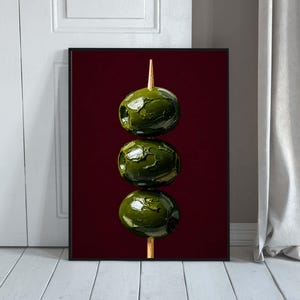 Può includere: Una stampa d'arte incorniciata che raffigura una pila verticale di tre olive verde scuro testurizzate, infilzate su uno spiedino di legno marrone chiaro. Le olive sono realizzate con pennellate spesse su uno sfondo bordeaux profondo.