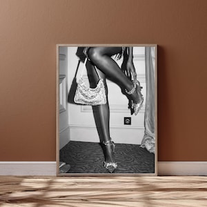 May include: Black and white framed print featuring a woman's legs, holding a sequined handbag and wearing embellished high heels. The image is set against a neutral background, with a focus on fashion and accessories.