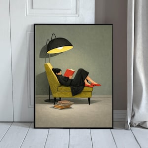 Puede incluir: Una lámina de arte enmarcada que muestra a una persona con ropa negra y zapatos rojos reclinada en un sillón amarillo, leyendo un libro rojo bajo una lámpara de pie negra. Una pila de libros descansa en el suelo junto al sillón ante una pared verde.
