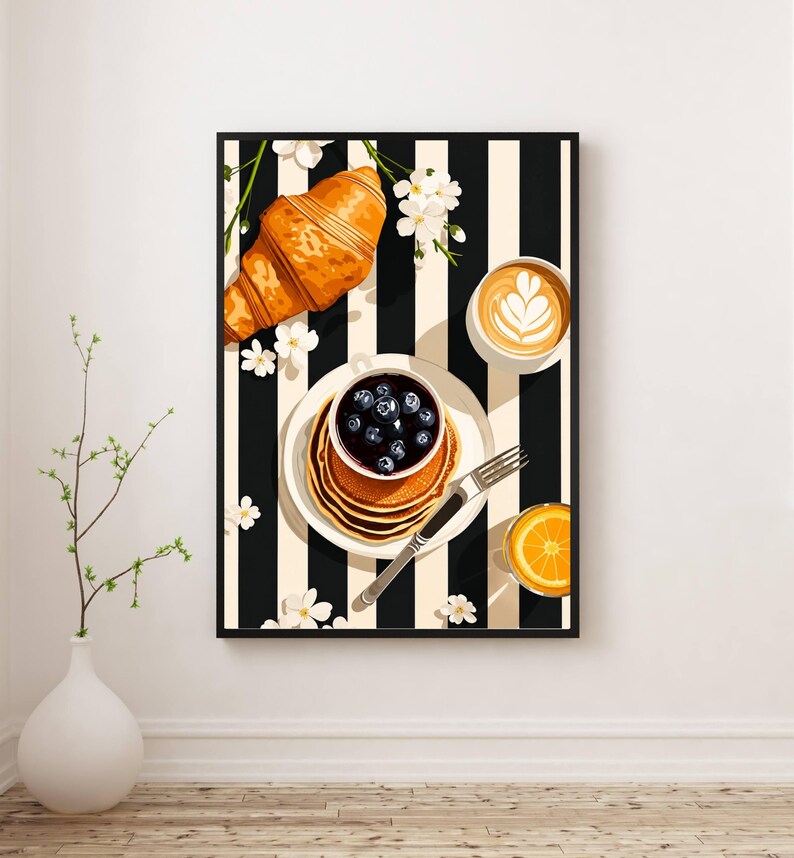Pu&ograve; includere: Una stampa d'arte incorniciata che raffigura una scena di colazione su uno sfondo a righe bianche e nere. L'immagine mostra un croissant dorato, una pila di pancake guarniti con mirtilli, una tazza con latte art e un bicchiere di spremuta.