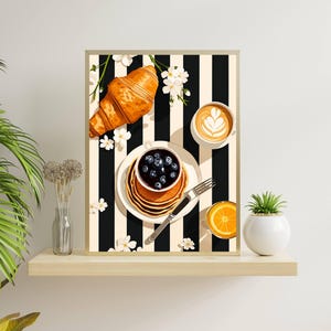Pu&ograve; includere: Una stampa artistica incorniciata raffigurante una scena di colazione con un croissant dorato, una pila di pancake con mirtilli, una tazza di caff&egrave; con latte art e un bicchiere di succo d'arancia su uno sfondo a righe verticali bianche e nere.